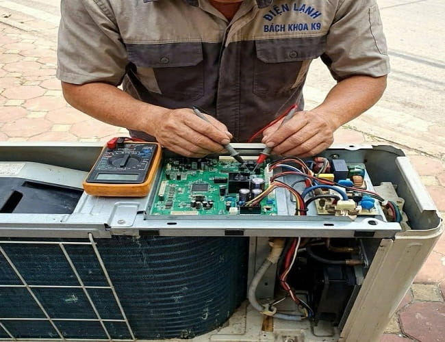Kỹ thuật viên đang sử dụng đồng hồ vạn năng để đo đạc, kiểm tra lỗi trên bo mạch điều khiển của điều hòa.